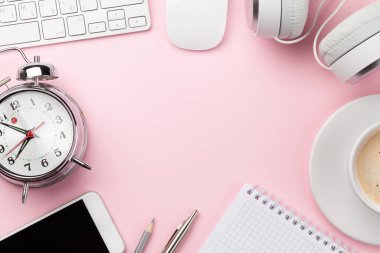 Üzerinde bilgisayar, malzeme, kahve fincanı ve çalar saat olan pembe çalışma masası. Sabah ya da teslim tarihi konsepti. Metnin için en üstte boşluk var. Düz yatıyordu
