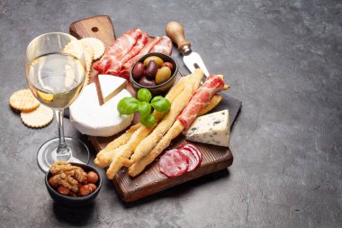 Peynir, et, üzüm ve fındıklı antipasto. Tabakta aperatif seçimi ve beyaz şarapla birlikte bardak. Kopyalama alanı ile