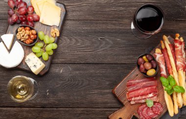 Peynir, et, üzüm ve zeytinli antipasto. Tahtada aperatif seçimi ve kırmızı beyaz şaraplı bardaklar. Kopyalama alanı olan üst görünüm. Düz yatıyordu