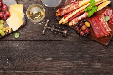 Peynir, et, üzüm ve zeytinli antipasto. Tahtada aperatif seçimi ve kırmızı beyaz şaraplı bardaklar. Kopyalama alanı olan üst görünüm. Düz yatıyordu