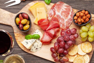 Peynir, et, üzüm ve zeytinli antipasto. Tahtada aperatif seçimi ve kırmızı beyaz şaraplı bardaklar. Üst Manzara. Düz yatıyordu