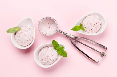 Kaselerde ahududulu dondurma kepçeleri ve pembe arka planda dondurma kaşığı. Üst görünüm düzlüğü