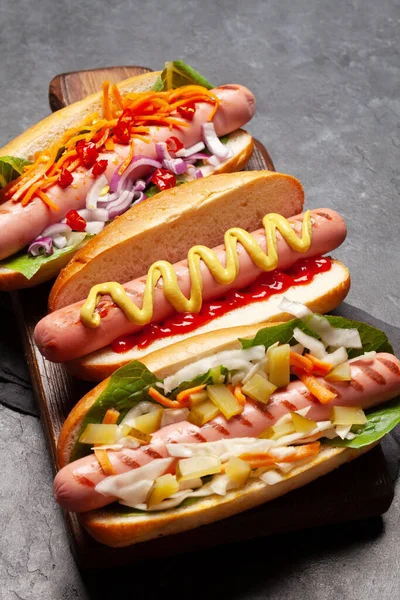 Various hot dog with vegetables, lettuce and condiments on stone background