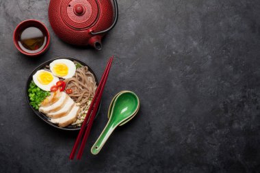 Tavuk, sebze, yumurta ve taştan arkaplanda bitki çayı ile Asya erişteli ramen çorbası. Üst görünüm düzlüğü kopyalama alanı ile yatıyordu