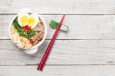 Asian noodle ramen soup with chicken, vegetables and eggs on wooden background. Top view flat lay with copy space