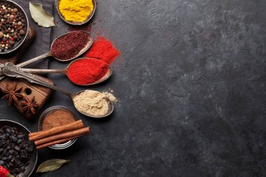 Koyu taş masada çeşitli baharatlar ve kaşıklar. Hint mutfağı. Üst görünüm düzlüğü kopyalama alanı ile yatıyordu