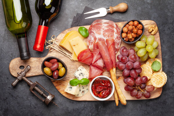 Cheese, meat, grapes and olives antipasto. Appetizer selection on wooden board with red and white wine. Top view. Flat lay