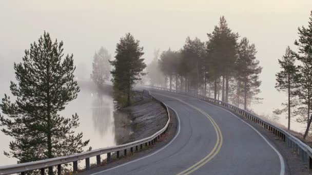 Paisaje finlandés con coches conduciendo en la niebla por carretera estrecha a través del lago — Vídeos de Stock