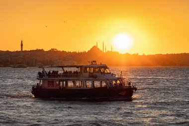 İstanbul, Türkiye 'de gün batımında feribot ve cami silueti yolcuları