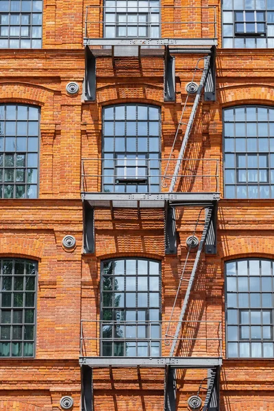 Red brick classic industrial building facade with fire escape ladder stairs — Stock Photo, Image