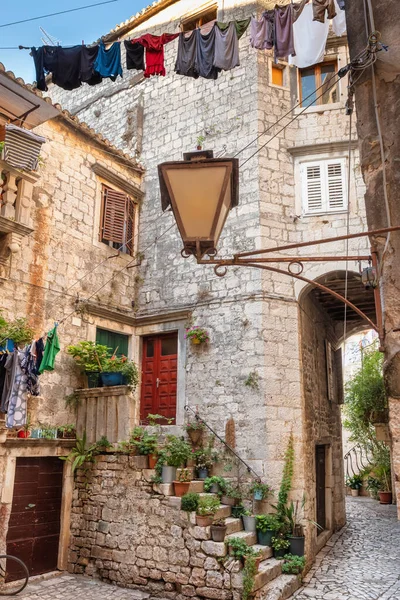 Trogir şehrinde çiçek saksıları ve kurutulmuş çamaşırları olan resim gibi dar bir cadde. — Stok fotoğraf