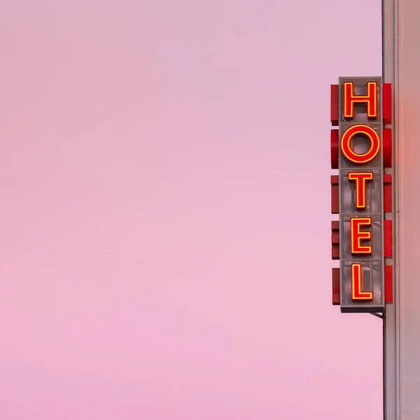 Neon hotel sign on the building corner with pink sunset sky at background. — Stock Photo, Image