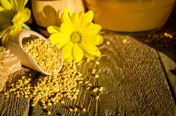 Granules de pollen d'abeille dans une cuillère en bois et fleurs sur une table en bois — Photo