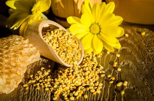 Granules de pollen d'abeille dans une cuillère en bois, des rayons de miel et des fleurs sur — Photo