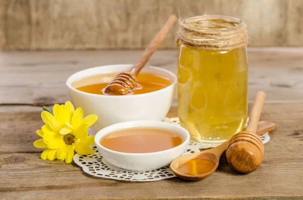 Gelbe Blume, Glas, Schüssel und Löffel mit Honig auf hölzernem Hintergrund — Stockfoto