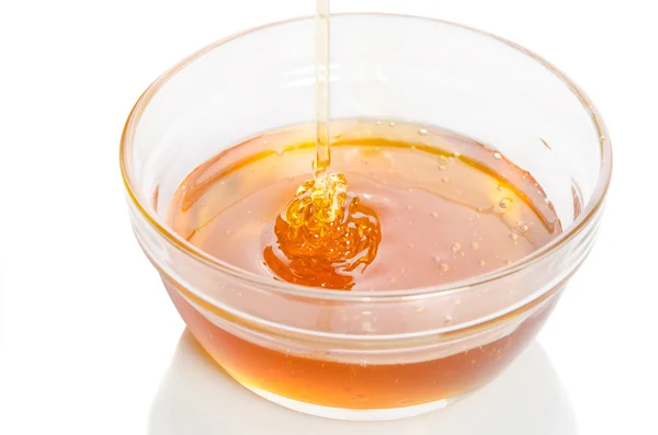 흰색 배경에 고립 된 유리 그릇에 물이 뚝뚝 떨어지는 꿀 — 스톡 사진