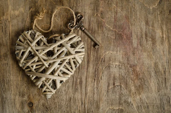Corazón de mimbre hecho a mano con la llave sobre una base de madera —  Fotos de Stock