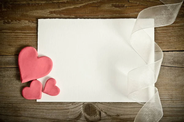 The piece of paper lying with hearts and ribbon on a wooden back — Stock Photo, Image