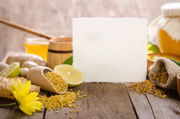 Favos de mel, mel, gengibre, pólen, limão em uma mesa de madeira com — Fotografia de Stock