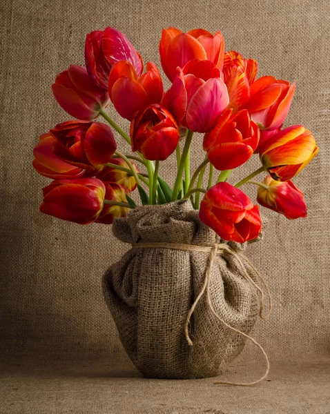 Beautiful bouquet of bright red tulips in a vase with burlap — Stock Photo, Image