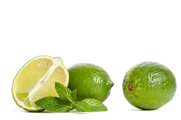 Två gröna limefrukter och mynta med hälften av saftig lime isolerad på w — Stockfoto