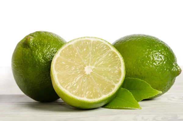 Två citroner med hälften av saftig lime på ett träbord — Stockfoto