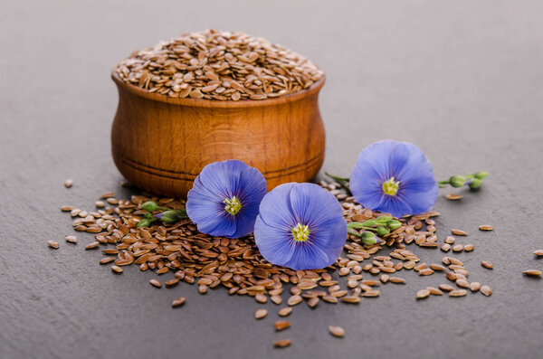 Flax seeds in the wooden bowl, beauty flower and oil in caps on 