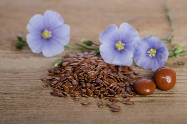 Flax seeds , beauty flower and pills on woooden background — Stock Photo, Image