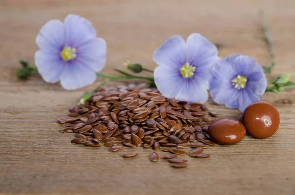 Semi di lino, fiore di bellezza e pillole su sfondo di legno — Foto Stock