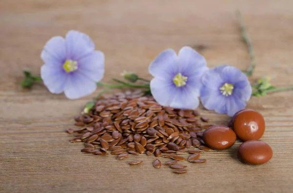 Flax seeds , beauty flower and pills on woooden background — Stock Photo, Image