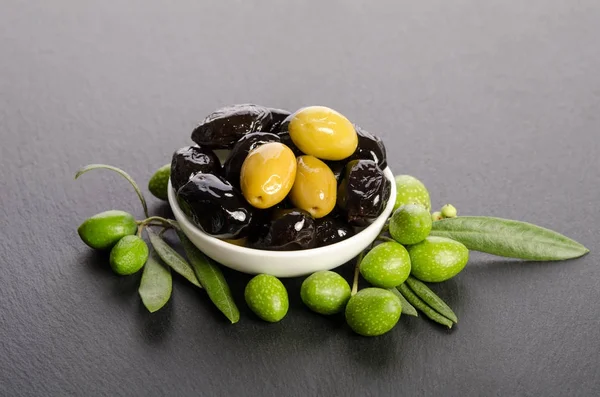 Černé a zelené olivy v porcelánové misce na šedý kámen — Stock fotografie