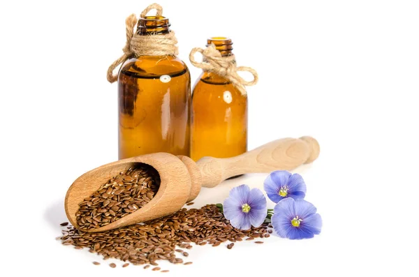 Semillas de lino en la cuchara de madera, botellas con aceite y flores de belleza —  Fotos de Stock