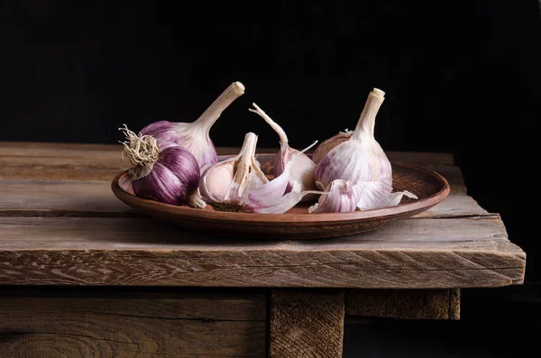 Garlic in the plate on old wooden table  and black background — Stock Photo, Image