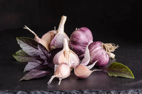 Leaves of basil and garlic on black stone table on black — Stock Photo, Image