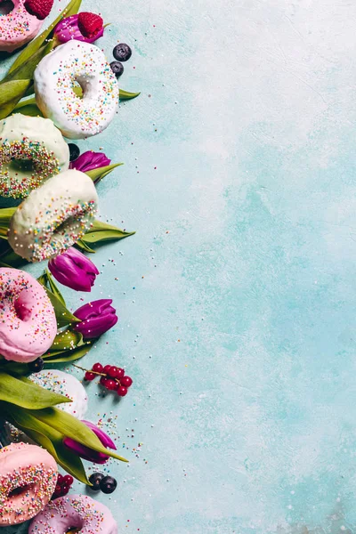 Donuts doces e coloridos com polvilhas, tulipas roxas e — Fotografia de Stock