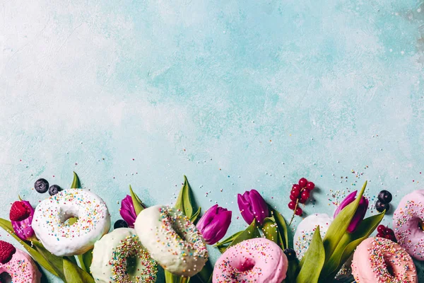 Donuts doces e coloridos com polvilhas, tulipas roxas e — Fotografia de Stock