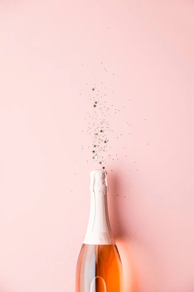 Champagne bottle with gold party streamers on pink background — Stock Photo, Image