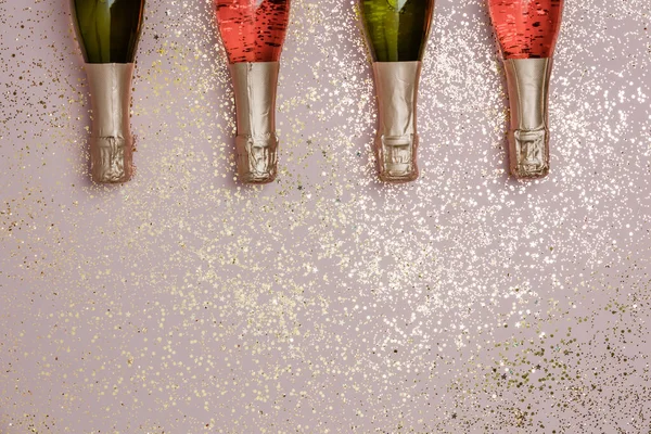 Láhve šampaňského se zlatými třpytkami, konfetami a prostorem pro text na růžovém pozadí — Stock fotografie