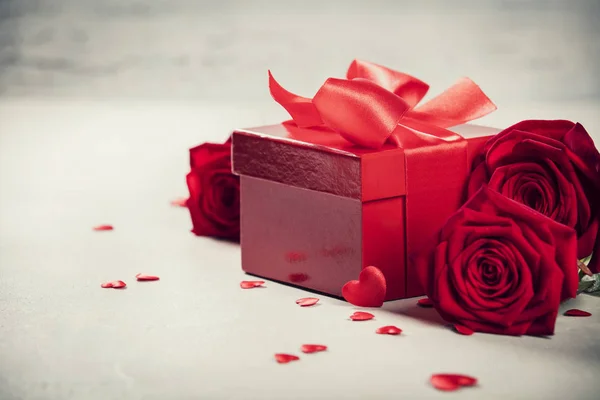 Koncepcja Walentynek. Walentynki pudełka związane z czerwoną satynową wstążką łuk i piękne róże na rustykalnym tle. — Zdjęcie stockowe