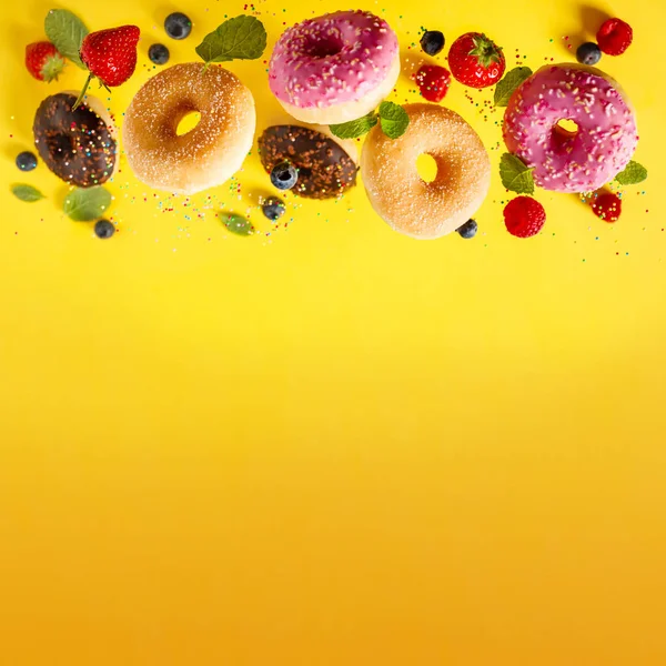 Various decorated doughnuts with sprinkles and berries in motion falling on yelloy background — Stock Photo, Image