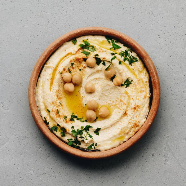 Large bowl of homemade hummus garnished with chickpeas, red sweet pepper, parsley and olive oil — Stock Photo, Image