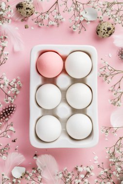 Beyaz seramik tutucu içinde yumurtalar ve pembe arka planda çiçekler, düz konum