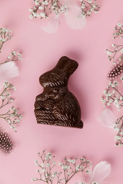 チョコレートイースターバニー、羽やパステルピンクの背景の花 — ストック写真