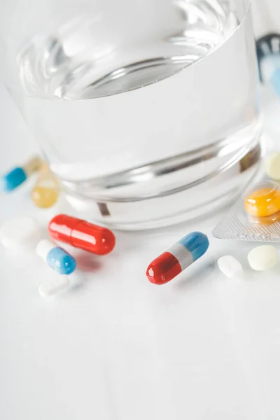 Medicin piller och kapslar med glas vatten på vit bakgrund. — Stockfoto