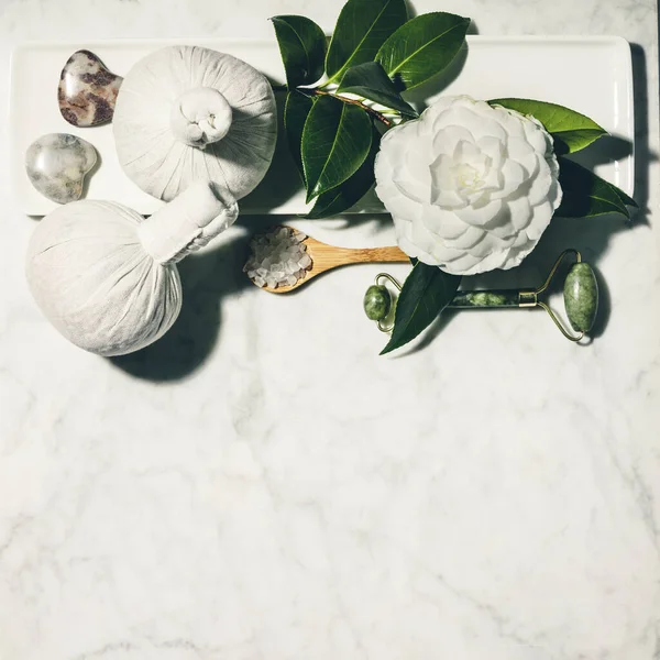 Composición laica plana con flor de camelia de primavera y varios productos de cuidado de la belleza en la mesa de mármol blanco — Foto de Stock