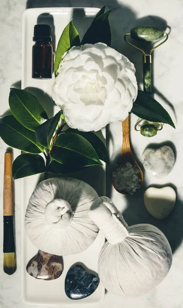 Composición laica plana con flor de camelia de primavera y varios productos de cuidado de la belleza en la mesa de mármol blanco —  Fotos de Stock