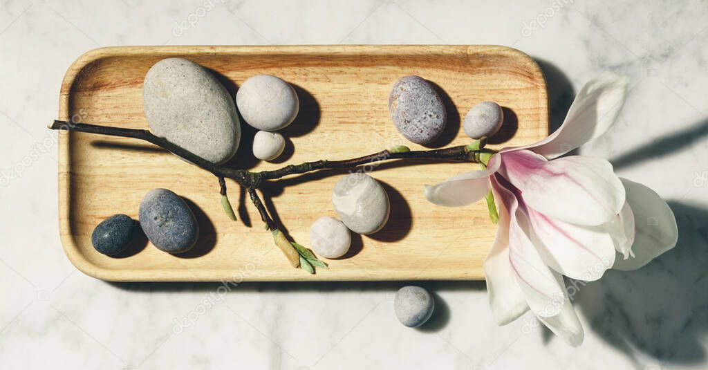 Flat lay composition with beautiful spring magnolia flowers and grey stones on white marble background. Relaxation and zen like concept.