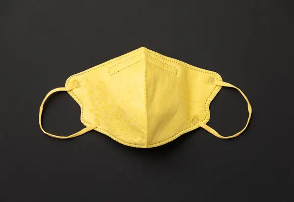 Žlutá lékařská maska na černém papíře pozadí byt ležel — Stock fotografie
