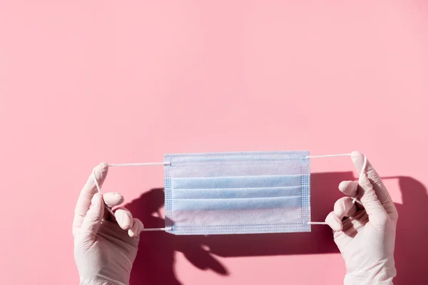 Woman hands in latex gloves holding facial medical mask, pink background, close up, copy space — Stock Photo, Image