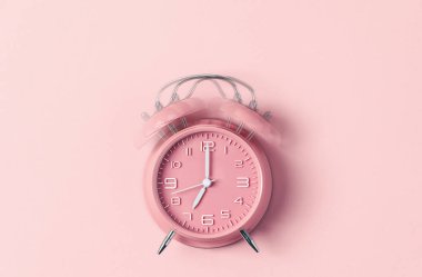 Klasik pembe alarmlı saat. Pastel pembe arka planda saat 7 'de çalıyor.